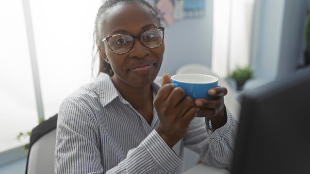 Woman drinking coffee in an office setting with a blue mug while wearing glasses and a striped shirt - Powered by Adobe