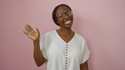 African american woman smiling and waving against a pink isolated background, exhibiting a cheerful...