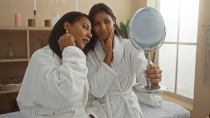 Obraz premium Mother and daughter in white bathrobes sharing a bonding moment while looking into a mirror in a cozy spa setting indoors