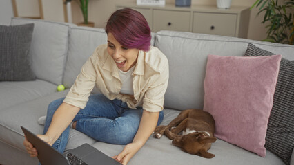 Obraz premium A young beautiful caucasian woman sits in her living room using a laptop with her dog sleeping beside her, creating a cozy and relaxed home environment.