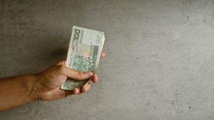 Hand holding polish zloty money against concrete wall background implies financial transaction in...