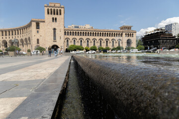 Obraz premium Visitors enjoy a sunny day at Republic Square in Yerevan, surrounded by striking buildings and serene water flows.