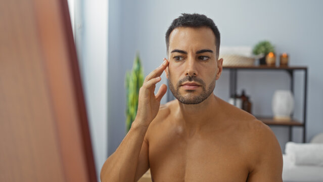 Handsome man with beard looking at his face in a spa room with wellness decor