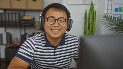 Handsome young chinese man smiling while wearing headphones in an indoor office setting.