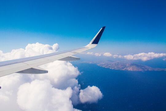 An airplane wing with clear blue sky background flying above Greek islands