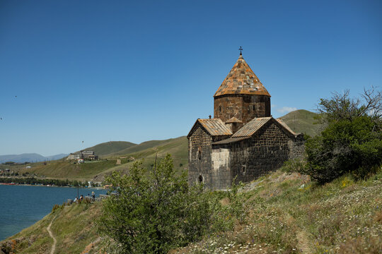 Sevanavank Monastery stands elegantly by Lake Sevan, embraced by lush greenery and hills under a bright blue sky.