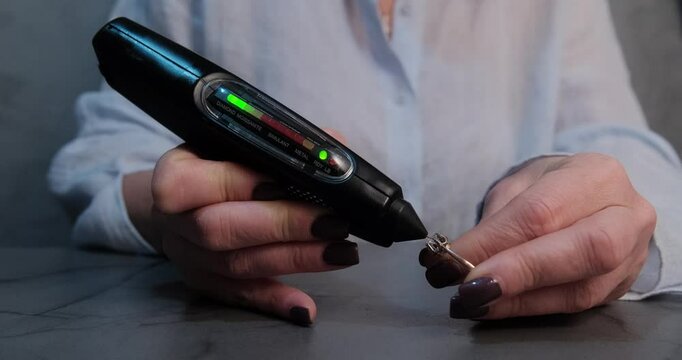 Detailed view of a jeweler using a handheld diamond tester to check the authenticity of a gemstone on a ring