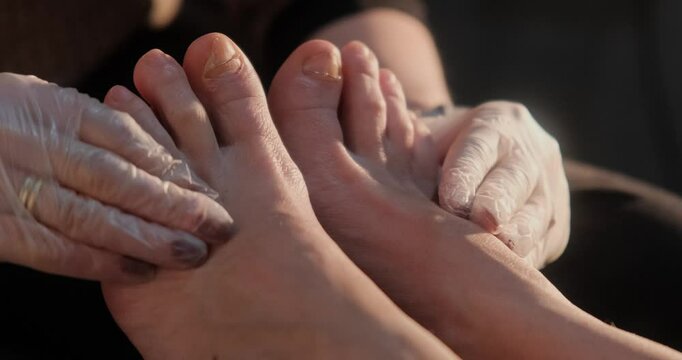 A professional podologist wearing gloves carefully treating a client's feet during a pedicure session, focusing on nail care and addressing potential fungal or nail issues