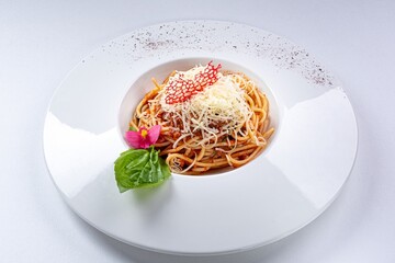 Bolognese Pasta with Parmesan, Basil Leaf, and Flower Garnish on a White Plate