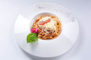 Bolognese Pasta with Parmesan, Basil Leaf, and Flower Garnish on a White Plate