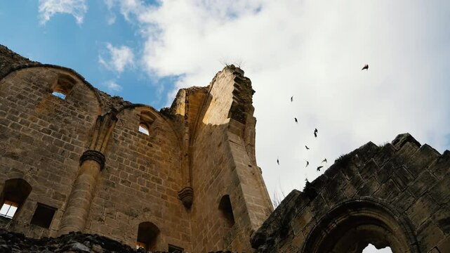 Slow motion panning of Bellapais ruins showing a birds flying in the sky behind the ruins.