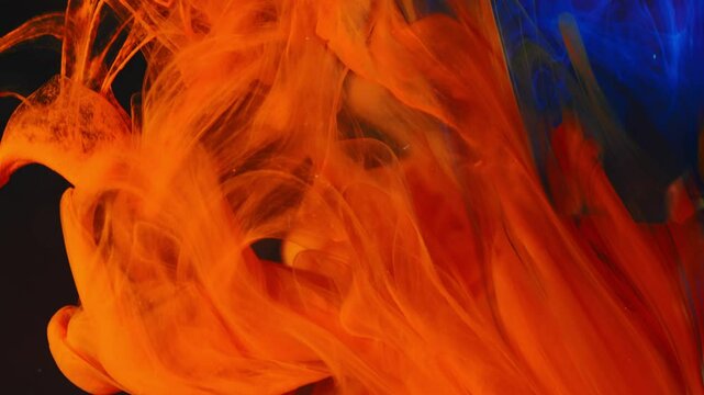 Orange ink flows into the water, mixing with blue ink. Abstract background