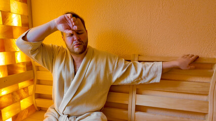 A Caucasian man in a sauna looks exhausted, illustrating the concept of stress relief and...