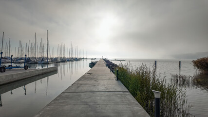 Obraz premium Misty morning at a tranquil marina with sailboats, perfect for concepts of solitude, reflection, and early morning calm
