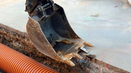 Excavator bucket positioned near orange utility pipe at construction site during daylight hours