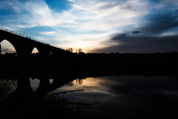 Silhouette of an Arched Bridge at Sunset Reflecting on Calm Waters in Fuentes Claras, Avila, CyL