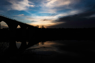 Silhouette of an Arched Bridge at Sunset Reflecting on Calm Waters in Fuentes Claras, Avila, CyL