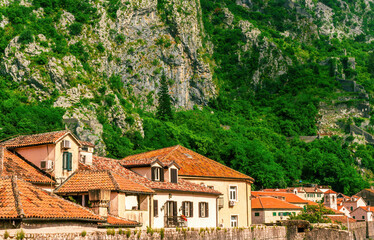 landscape of beautiful vintage houses with orange tile roofs in vintage venetian style to amazing high green mountain with ancient buildings on slopes and nice cloudy sky on background