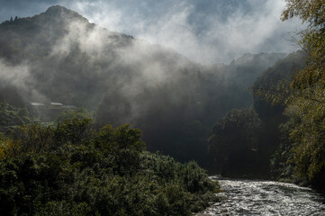 Fototapeta premium Misty mountain valley with a flowing river and forested hills in Shikoku, Japan.