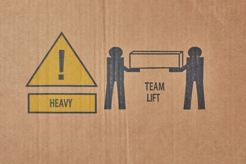 two shipping symbols printed on cardboard box, heavy and team lift icons with important handling...