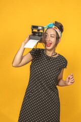 Beautiful Asian girl dressed in pin-up style with instant camera on bright yellow background. Isolated