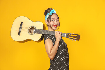 Beautiful Asian girl dressed in pin-up style with a guitar on a bright yellow background. Isolated. Close-up