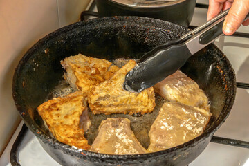 Pieces of fish are fried in boiling oil in an old cast-iron frying pan. Close-up
