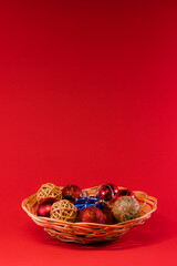 A wicker basket overflowing with an assortment of Christmas ornaments in red and gold, including...