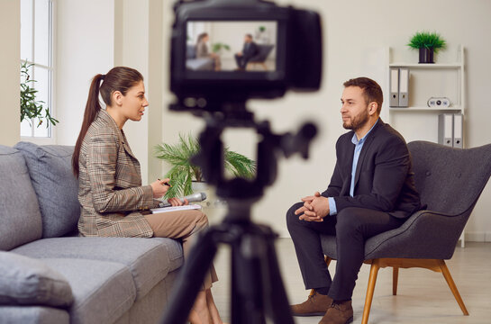 Close up photo of professional digital camera recording live podcast video interview of man and woman. Two bloggers podcasters talking with each other shooting live video sitting in studio.