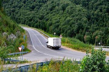 Cargo truck driving on a winding road surrounded by lush green forest.