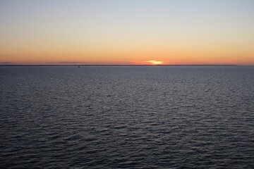 Die Sonne ist teilweise untergegangen &uuml;ber dem Kattegat an einem sch&ouml;nen Sommertag. Es gibt nur wenige Wellen, und die untergehende Sonne taucht den Himmel in orangefarbenes Licht.