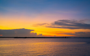 Obraz premium A stunning sunset over a calm sea. The sky is ablaze with vibrant hues of orange, yellow, and purple, while the water reflects the colors.