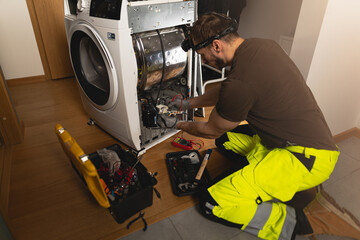 A repairman fixing a front-loading dryer, with tools scattered nearby