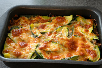 Casserole fresh from the oven with a orange brown cheese crust. Ingredients are zucchini, ground meat, potatoes, onions, garlic, cheese, and more.