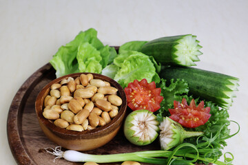 peanuts in a cup Place in a group of spring onions, brinjal, cucumber and green leafy vegetables. white background


