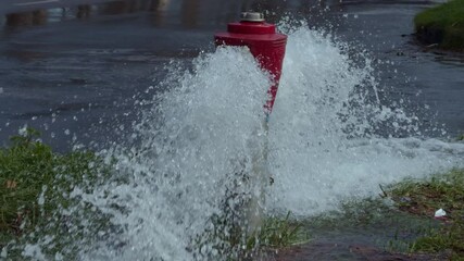 A burst fire hydrant causes water to spray across the street, highlighting urban infrastructure issues.