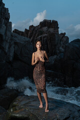 Beautiful Asian girl on the rocks by the sea posing in a leopard print dress at night