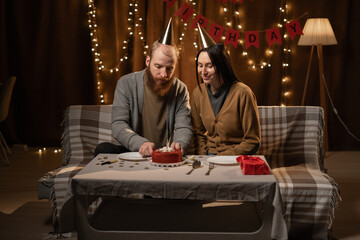 Husband's birthday. Wife surprise his husband with birthday cake. Anniversary. A young couple is at home, they are celebrating birthday. Couple celebrating holding a birthday cake