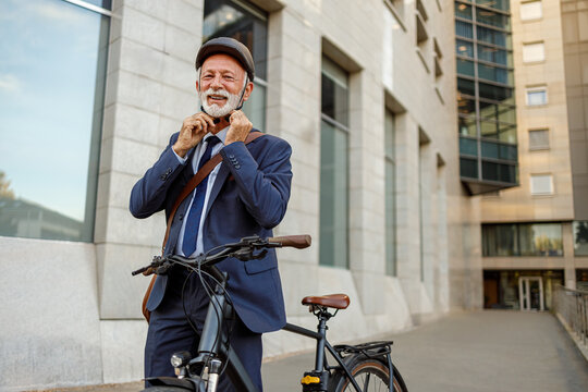 Portrait of smiling senior male commuter fastening helmet while going to work on bicycle in modern city