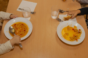 Dos niños comen un plato de garbanzos en la cafetería de un colegio público. alimentacion saludable