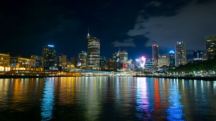 Fototapeta premium Vibrant skyline of a city at night featuring fireworks and colorful reflections on water, showcasing urban beauty and celebration.