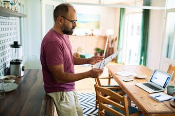 Man reviewing documents at home kitchen with laptop on table