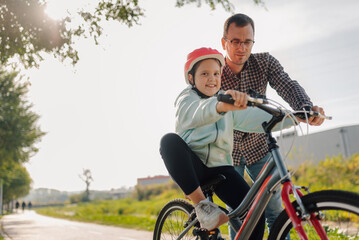 Obraz premium Father teaching daughter riding bicycle in park during sunny day