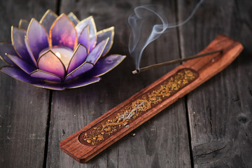 Burning incense stick on a wooden incense holder with golden ornaments and lotus flower candle....