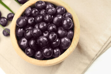 Ripe acai berries in bowl on white table, top view