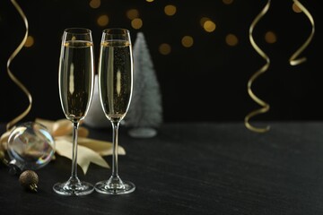 Delicious champagne in glasses and Christmas decor on black table against blurred lights, space for text
