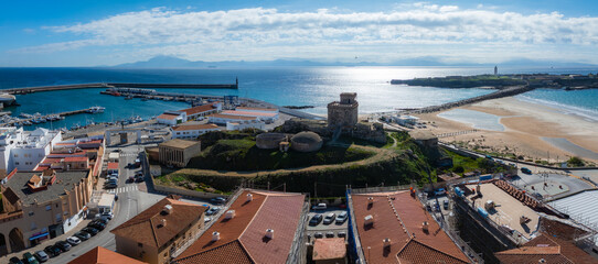 Tarifa's historic Guzman Castle stands amidst white buildings and a busy harbor. The sandy beach...