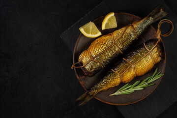 two hot smoked herrings with ropes and spices lie side by side on a clay plate on a stone cutting...