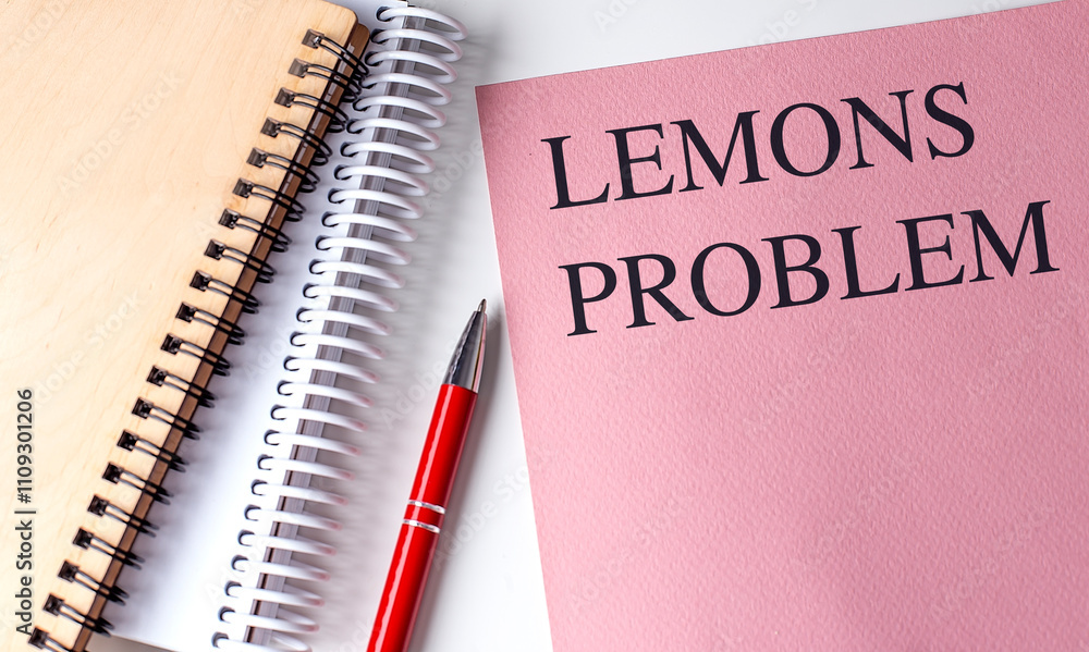 Poster notebook with the text lemons problem on a pink cover alongside other notebooks and a red pen