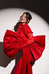 Radiant model in red dress, heels, and bow, beaming confidently in professional studio lighting